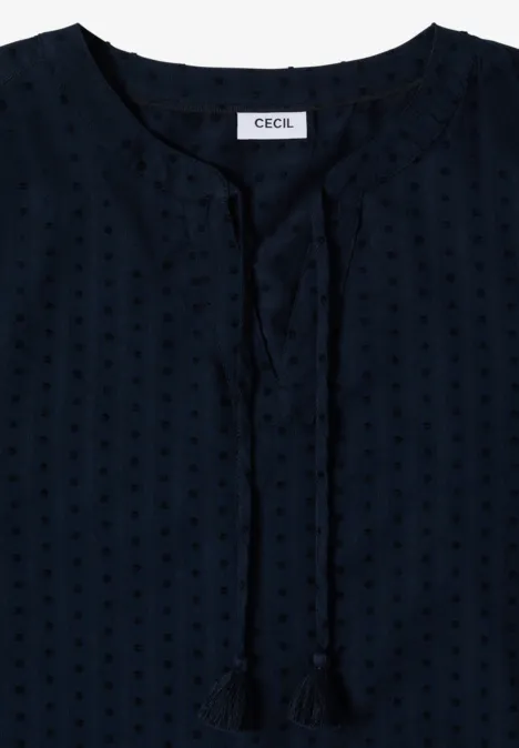 Dunkelblaue Damenbluse mit feinem Punktemuster, kurzem Stehkragen und dekorativen Quastenbändern.