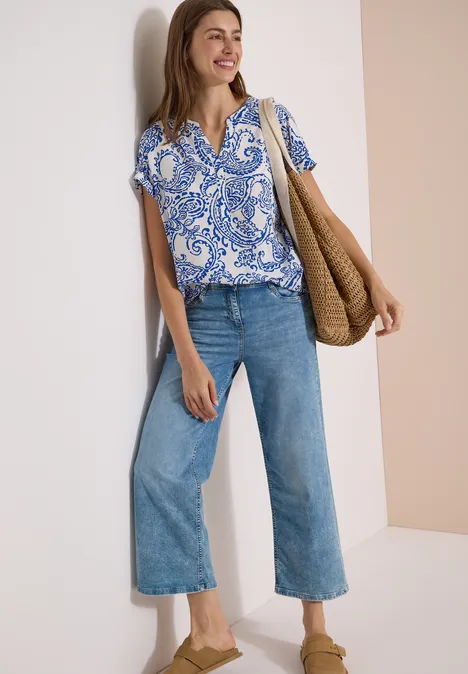 Blouse met split in de hals en print vanilla white Vrouw met blauw-wit motief blouse, wijde jeans, nude pumps en gevlochten tas.