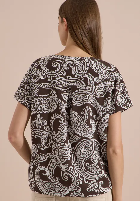 Blouse met split in de hals en print brown cacao Achteraanzicht van een vrouw in een loszittend zwart-wit paisley-print T-shirt met korte mouwen.