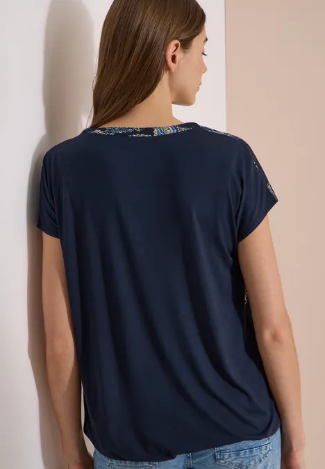 Blouse met split in de hals en een mix van texturen universal blue Vrouw van achteren draagt een donkerblauw T-shirt met korte mouwen voor een lichte muur.
