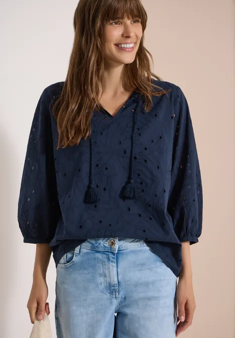 Frau trägt dunkelblaue Lochstickerei-Bluse mit V-Ausschnitt und Jeans.