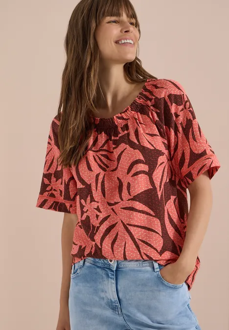 Carmen-Bluse mit Kurzarm und Blätterprint coral Frau trägt rotes, gemustertes Kurzarmshirt und blaue Jeans.