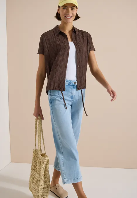 Frau trägt hellblaue Culotte-Jeans, weißes Top, braunes Kurzarmhemd und geflochtene Tasche.