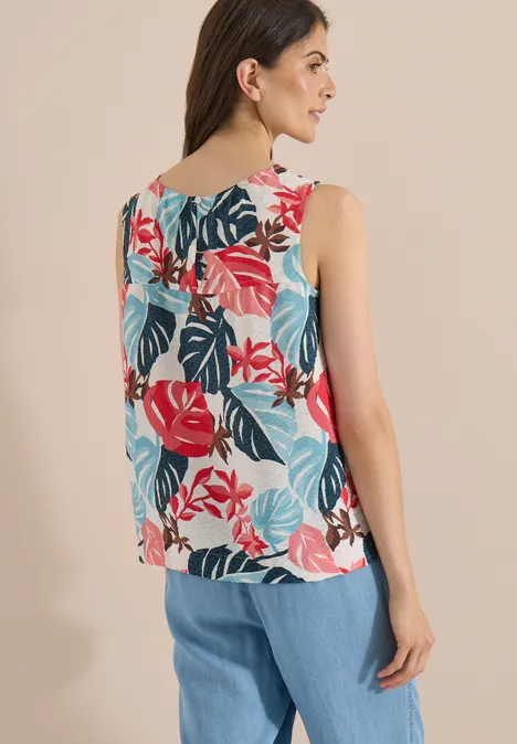 Vrouw van achteren in een mouwloze top met kleurrijke bladprint en wijde blauwe broek.