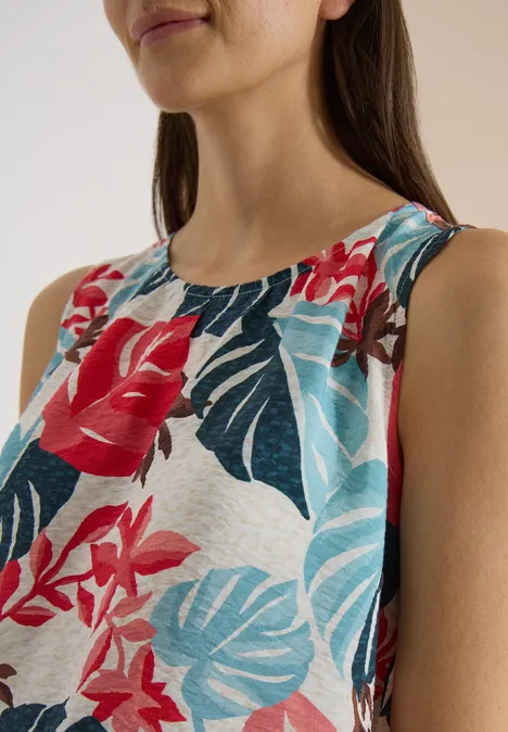 Vrouw draagt mouwloos topje met kleurrijke bloemen- en bladerenprint.