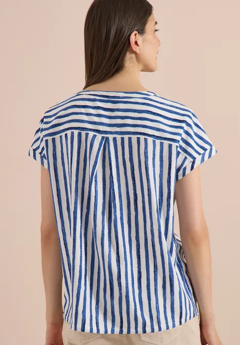 Frau von hinten in weiß-blau gestreiftem Kurzarmshirt vor beigem Hintergrund.