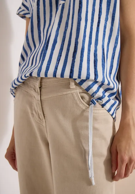 Person trägt beige Hose und blau-weiß gestreiftes Shirt, sichtbare Hände und ein hängender Kordelzug.