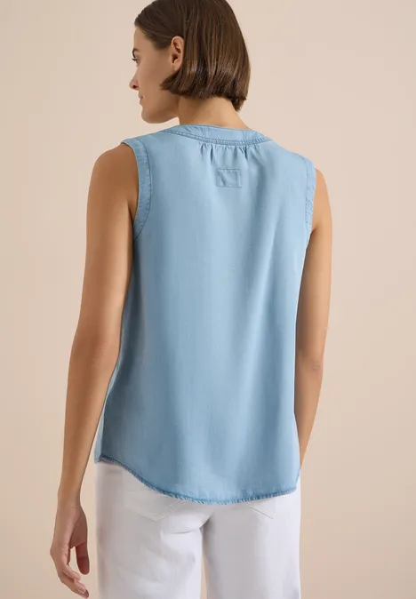 Frau von hinten in ärmellosem hellblauem Denim-Top und weißen Hosen.