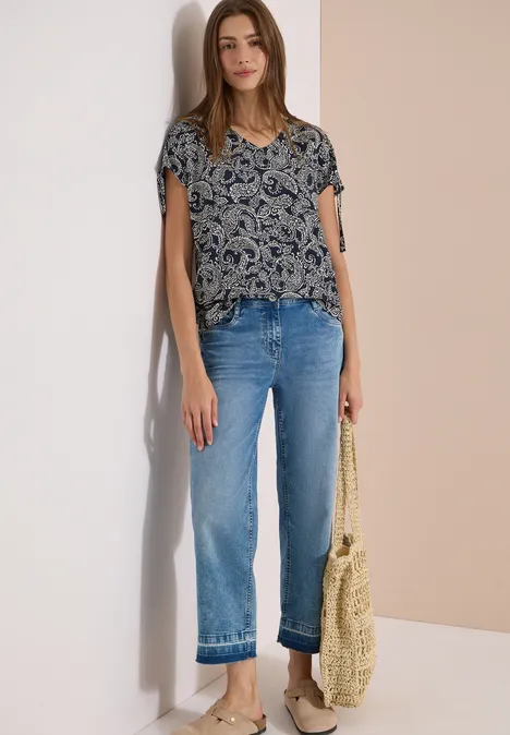 Overhemd met gerimpeld detail universal blue Vrouw in rechte jeans, kort mouwtop met print en gevlochten tas, staand voor een lichte achtergrond.