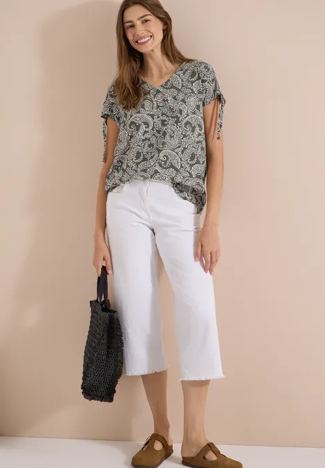 Overhemd met gerimpeld detail khaki Vrouw draagt een shirt met print, witte culotte, bruine loafers en een zwarte gevlochten tas, neutrale achtergrond.