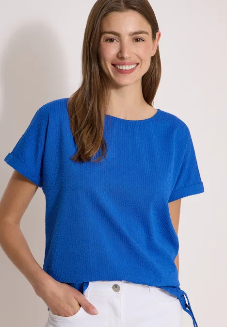 Blouse met ronde hals en knoopdetail surf blue Vrouw in blauw kort t-shirt met ronde hals, staand voor een lichte achtergrond.