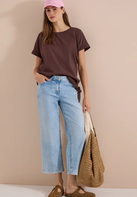 Blouse met ronde hals en knoopdetail brown cacao Vrouw met bruin T-shirt, lichte wijde jeans en een grote gevlochten tas.