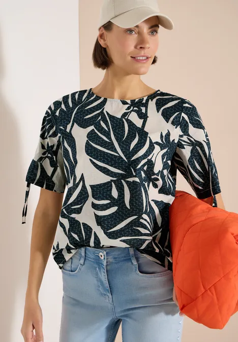 Blouse avec col rond et fronces palm breeze green Femme en t-shirt blanc à motif feuilles bleues, jean clair et grand sac orange.