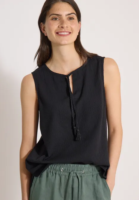 Ärmellose schwarze Bluse mit Band am Ausschnitt, locker in grüne Hose gesteckt.