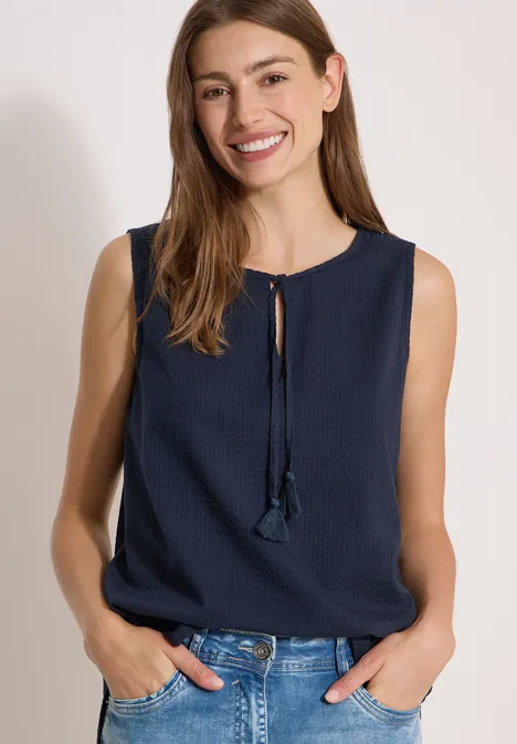 Blusentop mit Split Neck und Bändern universal blue Frau in ärmellosem marineblauen Top mit Quasten, steht locker mit Händen in Hüfttaschen.