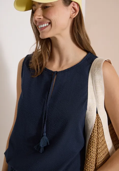 Blusentop mit Split Neck und Bändern universal blue Frau trägt ärmellose dunkelblaue Bluse mit Quasten und zwei Schultertaschen aus Bast und Canvas.