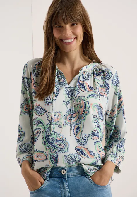 Eine Frau trägt eine Bluse mit buntem Paisley-Muster und V-Ausschnitt.