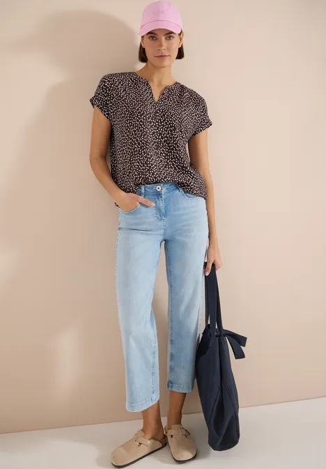 Femme porte un top à motif manches courtes, jean droit bleu clair, mocassins beiges et un sac fourre-tout bleu marine.