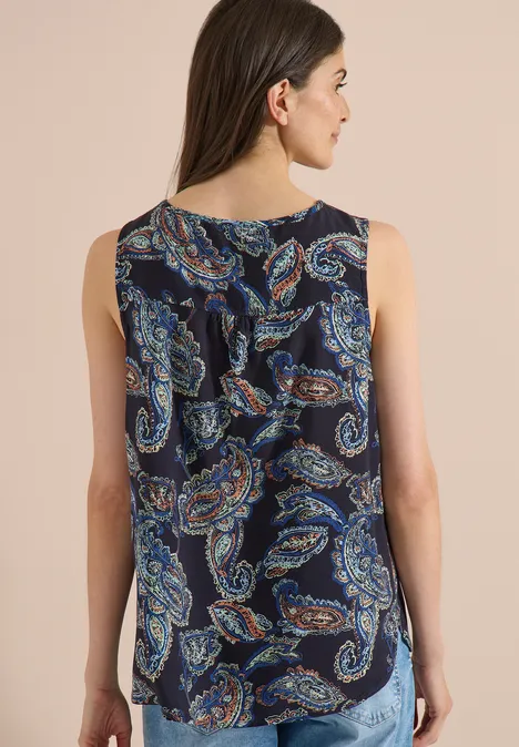 Rückenansicht einer Frau in ärmelloser Bluse mit rundem Ausschnitt und buntem Paisley-Muster auf dunklem Grund.