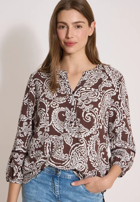 Tuniek met 3/4-mouwen en print brown cacao Dame draagt een bruine paisley blouse met V-hals en een blauwe jeans.