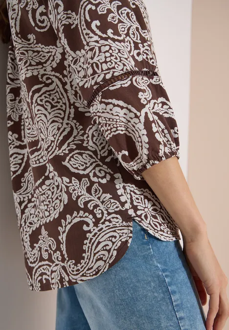 Tuniek met 3/4-mouwen en print brown cacao Zijdelingse opname van een bruin hemd met wit paisleypatroon en blauwe jeans.