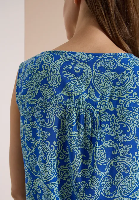 Rückansicht einer Person in ärmellosem, blauem Oberteil mit grünem Paisley-Muster.
