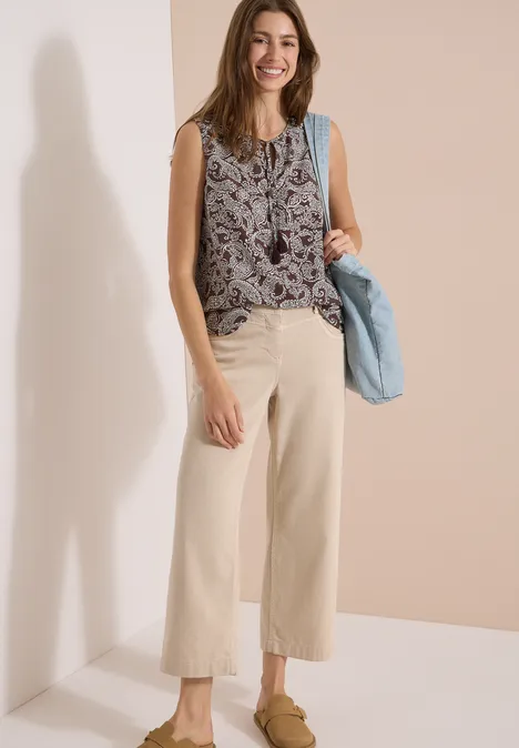 Femme en top sans manches à motifs, pantalon ample clair et sac à main bleu.
