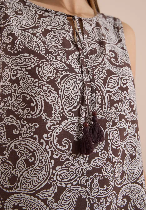 Top marron sans manches à motif paisley blanc avec pompons au niveau de l'encolure.