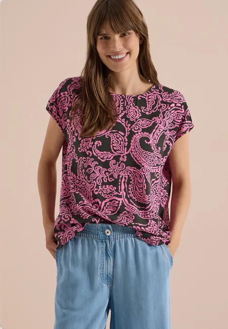 Blusenshirt mit Rundhals und Print raw khaki Frau trägt pink gemustertes T-Shirt und hellblaue Jeanshose, steht mit Händen in den Taschen.