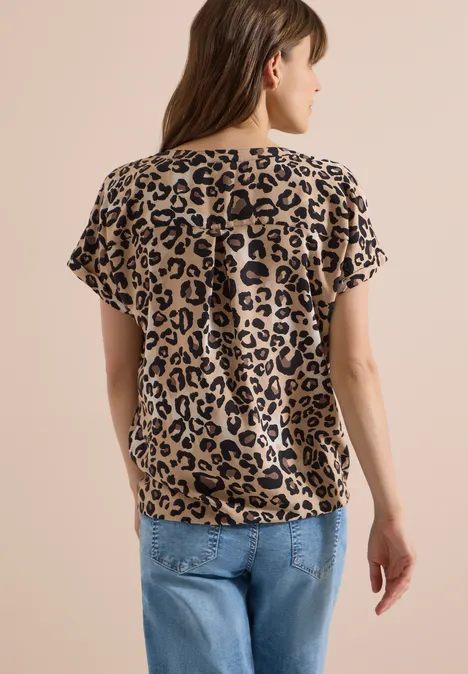 Rückansicht einer Frau in beiger Leo-Print-Bluse und blauen Jeans.
