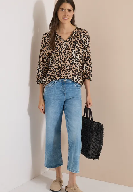 Frau trägt eine locker sitzende Leopardenbluse, hellblaue Cropped-Jeans und eine schwarze Flecht-Tasche.