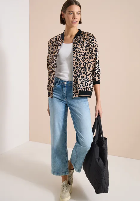 Leichter Blouson mit Zipper und Leo-Print urban taupe Frau in Leopardenjacke, weißem Top, weiten Jeans und Sneakern trägt eine schwarze Stofftasche.
