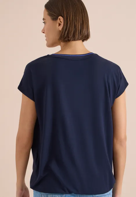 Rückenansicht einer Frau mit schulterlangem Haar, in dunkelblauem, kurzärmeligem T-Shirt.