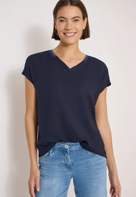 Frau trägt ein dunkelblaues V-Ausschnittshirt mit überschnittenen Schultern und blaue Jeans