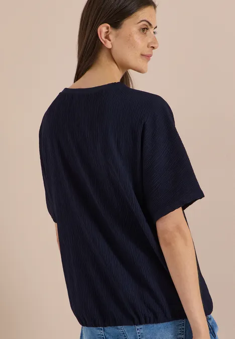 Chemisier à épaules tombantes, couleur unie urban dark blue Frau im Profil trägt dunkelblaues T-Shirt vor neutralem Hintergrund.