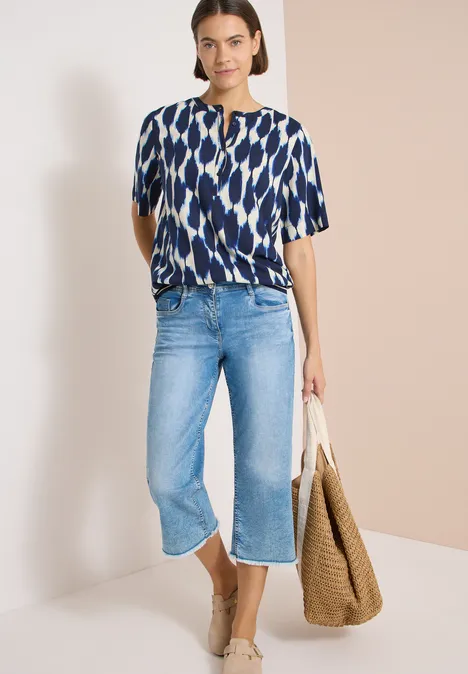Frau mit gemustertem Oberteil, weiten blauen Culotte-Jeans und großem Korbtasche.