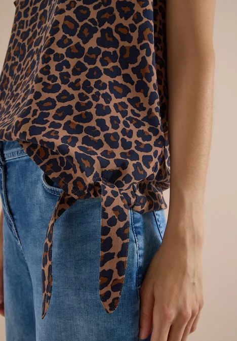 Chemisier à épaules tombantes avec nœud creamy mocha Feminines Leopardenmuster-Oberteil mit Knoten am Saum, kombiniert mit blauen Jeans.