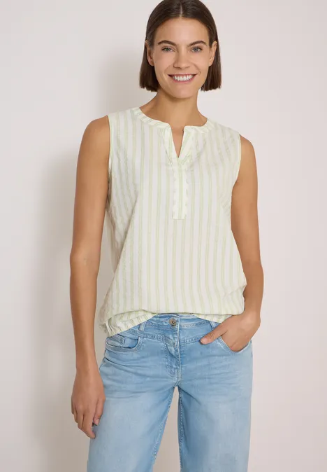 Seersucker Blusentop mit Streifen raw matcha lime Frau in hellgelb-weiß gestreiftem Top und Jeans, lächelt entspannt in legerer Pose.