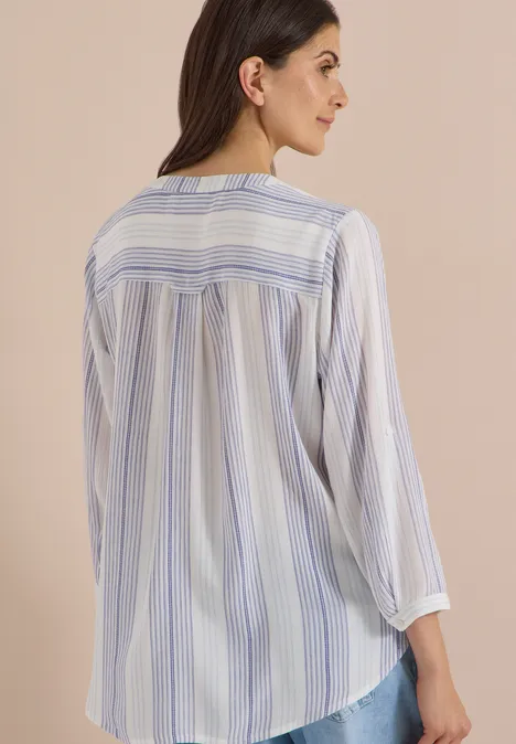 Frau im gestreiften Blusenshirt sitzt seitlich, blaue und weiße Streifen.