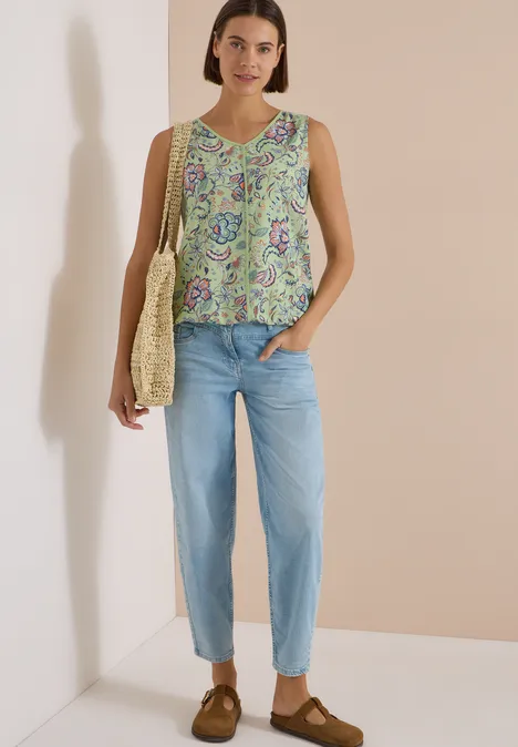 Blusentop mit V-Neck und Print raw matcha lime Eine Frau trägt ein ärmelloses, geblümtes Top, hellblaue Jeans, braune Schuhe und eine Korbtasche.