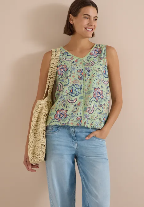 Blusentop mit V-Neck und Print raw matcha lime Lächelnde Frau mit ärmellosem Top im Paisley-Muster, Jeans und sommerlicher Strohtasche.