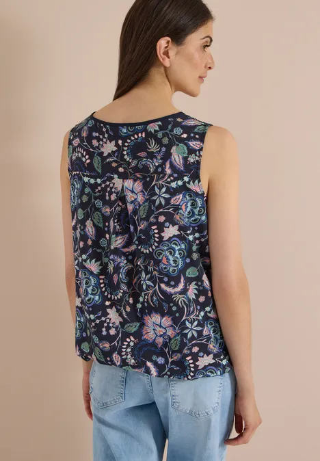 Eine Frau von hinten trägt ein ärmelloses, dunkelblaues Top mit buntem Blumenmuster und helle Jeans.