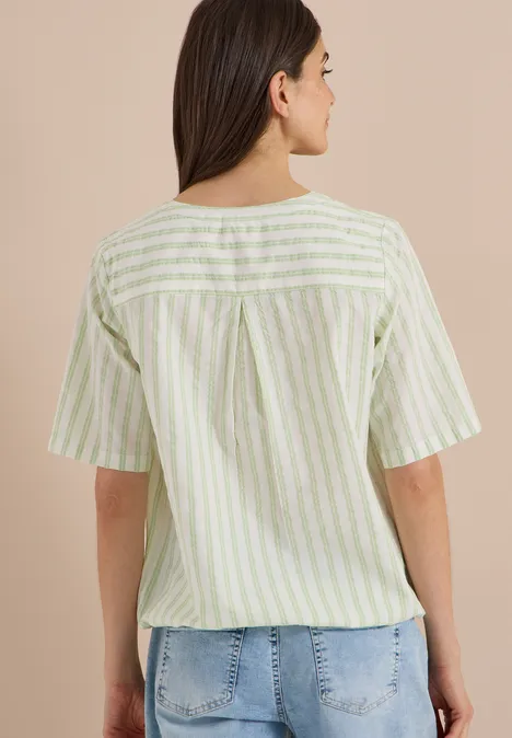 Chemisier à manches courtes, à col fendu et rayures raw matcha lime Frau von hinten in grün-weiß gestreifter Bluse und Jeans.