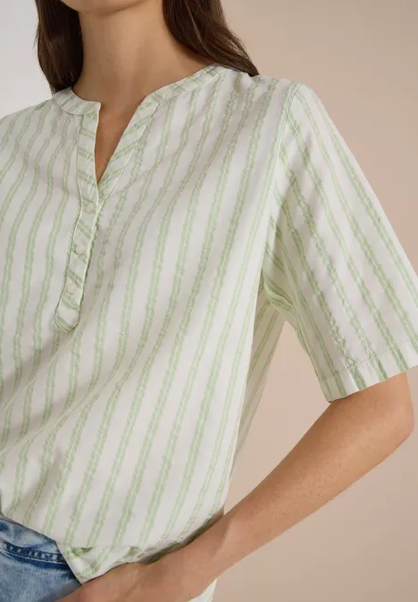 Chemisier à manches courtes, à col fendu et rayures raw matcha lime Frau in locker geschnittener, hellgrün-weiß gestreifter Bluse mit kurzen Ärmeln, lässig in Jeans gesteckt.