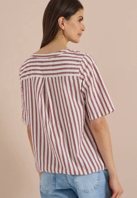 Chemisier à manches courtes, à col fendu et rayures russet red Frau von hinten in gestreiftem Kurzarmshirt und Jeans vor neutralem Hintergrund.