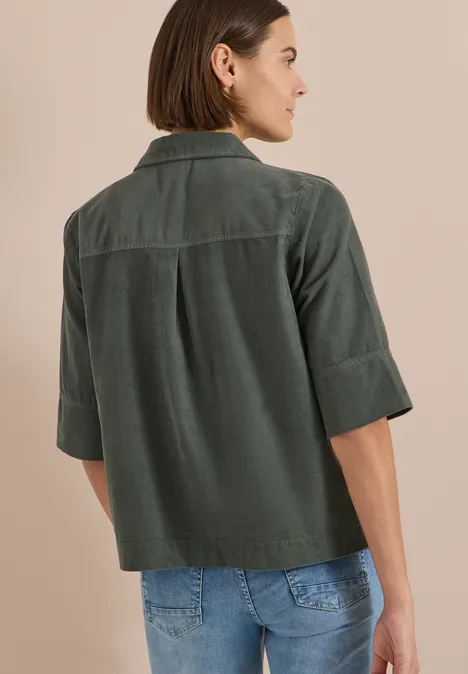 Overhemd met korte mouwen van corduroy met borstzak dried olive green Frau von hinten, trägt grüne Cord-Hemdjacke mit Ellbogenärmeln und blaue Jeans.