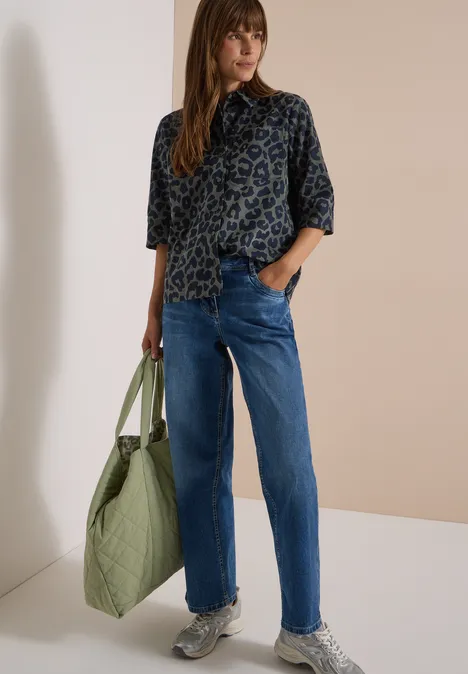 Overhemd met korte mouwen van corduroy met luipaardprint dried olive green Vrouw in leopardprint blouse, blauwe jeans, sneakers, draagt grote groene tas