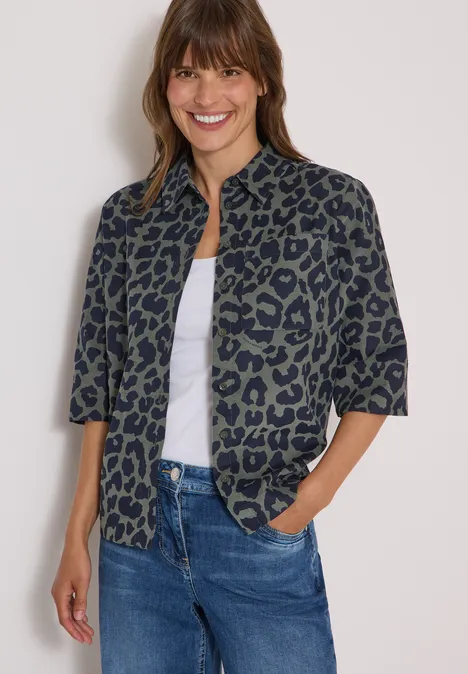 Overhemd met korte mouwen van corduroy met luipaardprint dried olive green Een lachende vrouw in een groene blouse met luipaardprint, wit topje en spijkerbroek.