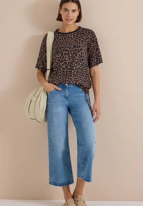 Blouse met korte mouwen en luipaardprint creamy mocha Eine Frau trägt eine Leo-Bluse, weite Jeans-Culotte und helle Tasche vor beigem Hintergrund.