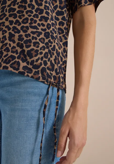 Blouse met korte mouwen en luipaardprint creamy mocha Nahaufnahme eines Unterkörpers in blauer Jeans und Leopardenmuster-Bluse mit seitlichen Schnürungen